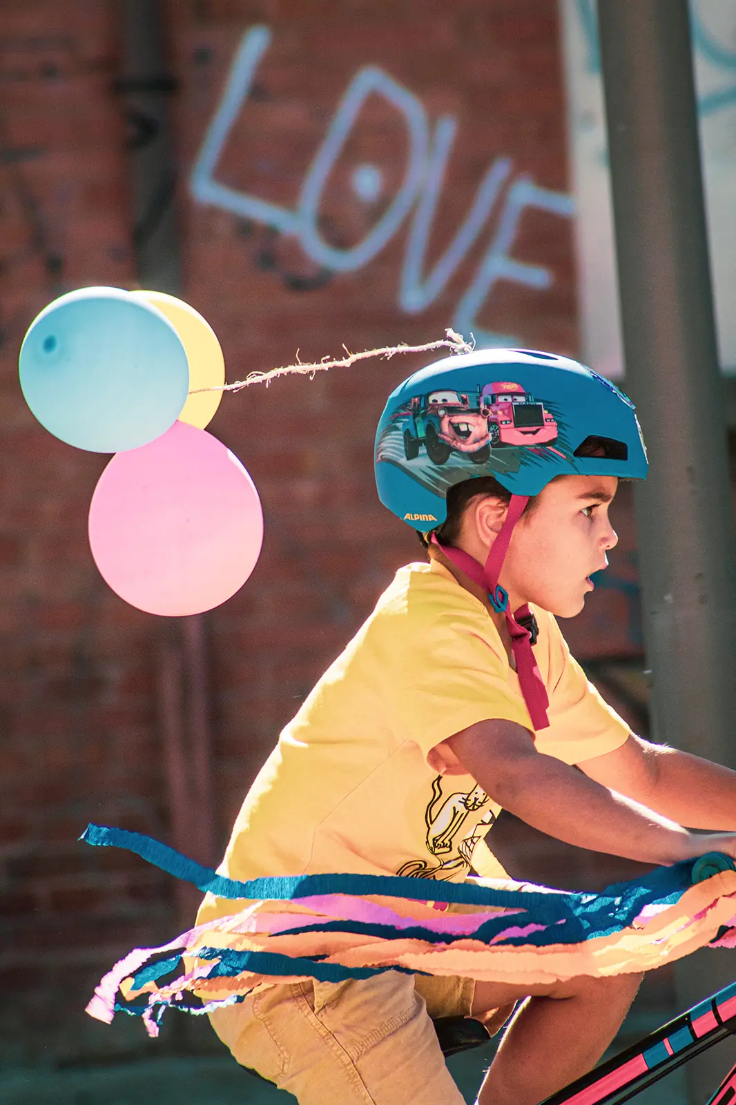 Bambino in bici con palloncini colorati legati al casco